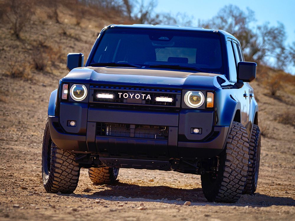 Blue Toyota Prado 250 on a dirt road with a clear sky and Lazer Lamps ST4 Evolution Grille Kit – Land Cruiser 250 (2024+)