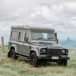 Land Rover Defender in a grassy field with a mountainous background
