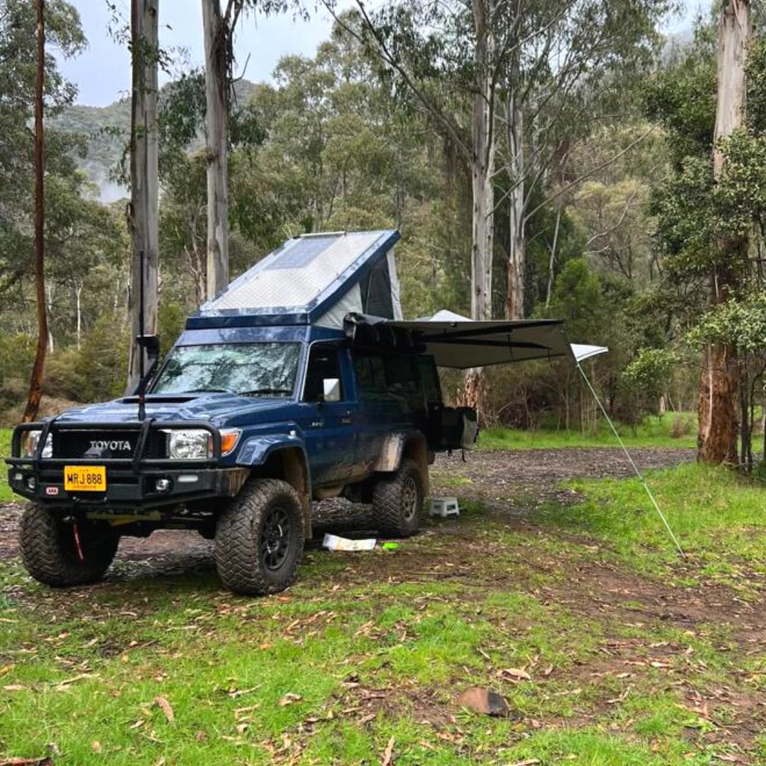 Blue Toyota truck with a camper shell parked in a forested area