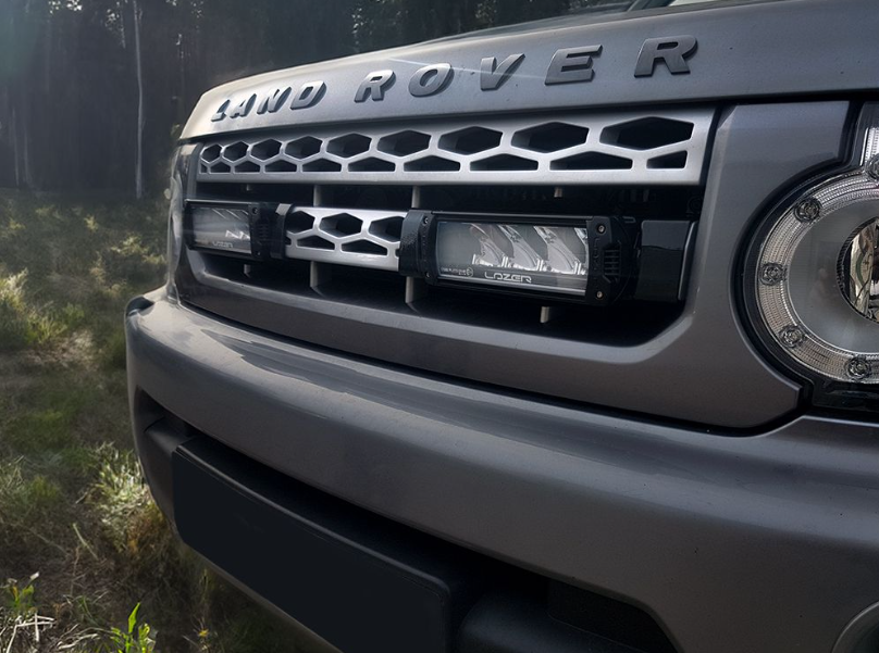 Close-up of a Land Rover vehicle's front grille and headlight in a forest setting