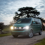 Green Volkswagen van on a gravel driveway with trees and a cloudy sky in the background