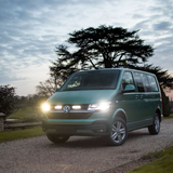 Green Volkswagen van on a gravel driveway with trees and a cloudy sky in the background