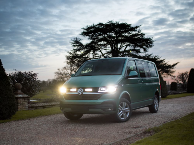 Green Volkswagen van on a gravel driveway with trees and a cloudy sky in the background