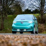 Turquoise electric car on a road with trees and grass in the background with Lazer Lamps Grille Kit for VW ID Buzz (2025+)