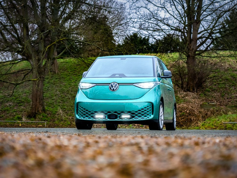 Turquoise electric car on a road with trees and grass in the background with Lazer Lamps Grille Kit for VW ID Buzz (2025+)