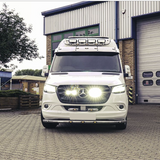 White Mercedes-Benz van parked in front of a building with a garage door with Lazer Lamps Mercedes Sprinter (2018+) Grille Kit
