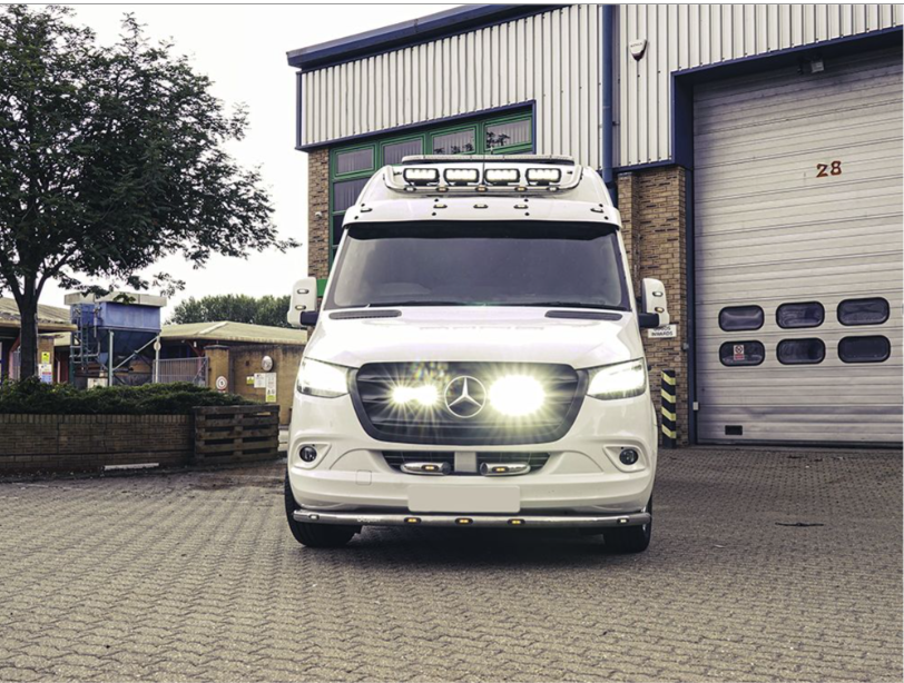 White Mercedes-Benz van parked in front of a building with a garage door with Lazer Lamps Mercedes Sprinter (2018+) Grille Kit