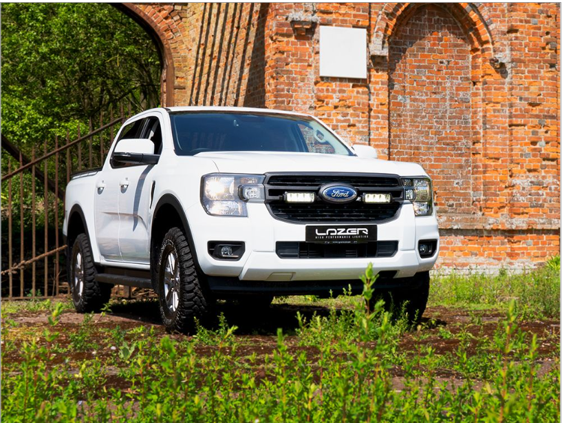 White Ford Lazer truck parked in front of a brick wall with greenery.