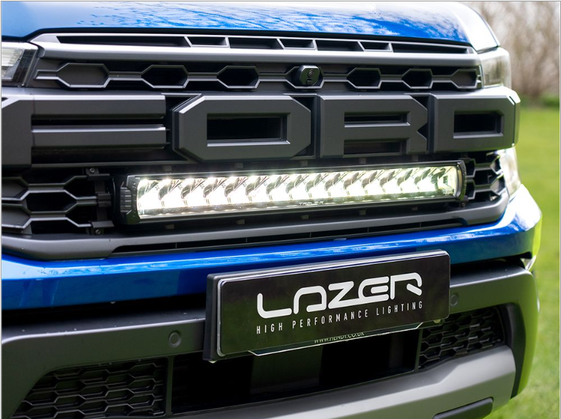 Close-up of a Ford vehicle grille with LazerLamps Raptor Grille Kit, on a grassy background.