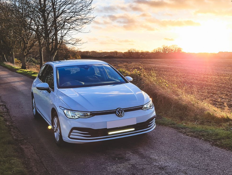 White Volkswagen car on a rural road with sunset in the background