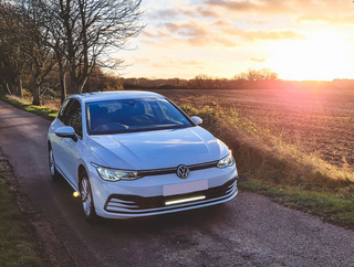 White Volkswagen car on a rural road with sunset in the background