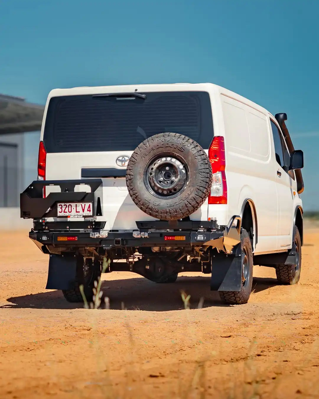 White van with a spare tire mounted on the back, parked on a dirt road.