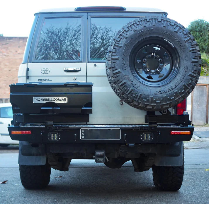 Back view of a white Toyota Land Cruiser with a spare tire mounted on the back, parked on a street.