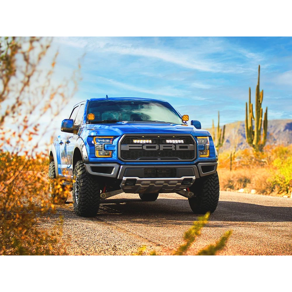 Blue F150 raptor truck on a desert road with cacti and mountains in the background with Lazer Lamps Grille Kit – Ford F-150 Raptor (2017–2020)