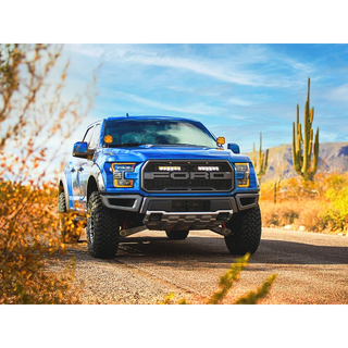 Blue F150 raptor truck on a desert road with cacti and mountains in the background with Lazer Lamps Grille Kit – Ford F-150 Raptor (2017–2020)