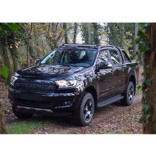 Black pickup truck parked in a forested area with Lazer Lamps Roof Mount Kit – Ford Ranger (2016–2022 with Roof Rails)