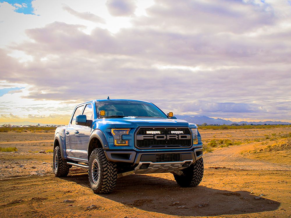 Blue Ford truck on a desert road with a cloudy sky