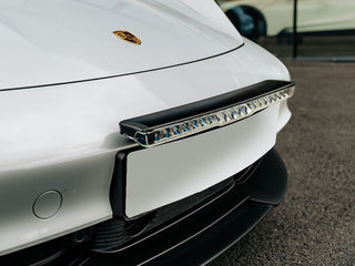 Close-up of a car's front bumper with a Lazerlamps Licence Plate Mount (Glide) on a white car.