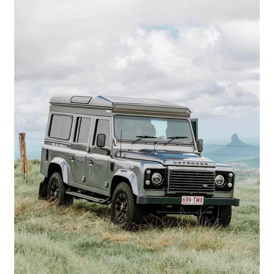 Land Rover Defender in a grassy field with a mountainous background – Headspace Roof Conversion D90/110