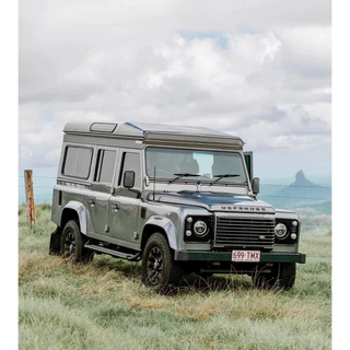 Land Rover Defender in a grassy field with a mountainous background – Headspace Roof Conversion D90/110