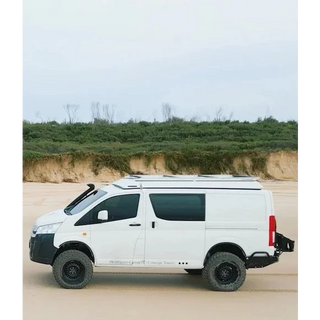 White van modified for off-road use on a sandy terrain with greenery in the background – Headspace Roof Conversion HiAce