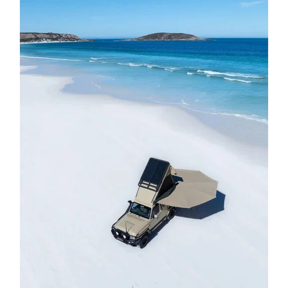 Beige off-road vehicle with a roof rack on a sandy beach with blue ocean and sky.