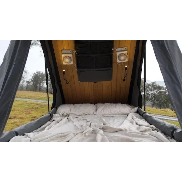Bed inside a camper van with wooden paneling and curtains, outdoors – Headspace Roof Conversion LC76