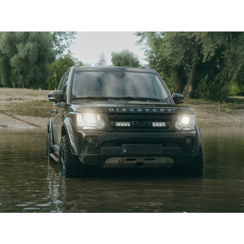 Land Rover Discovery driving through water with trees in the background