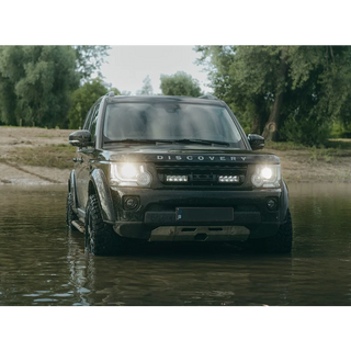 Land Rover Discovery driving through water with trees in the background