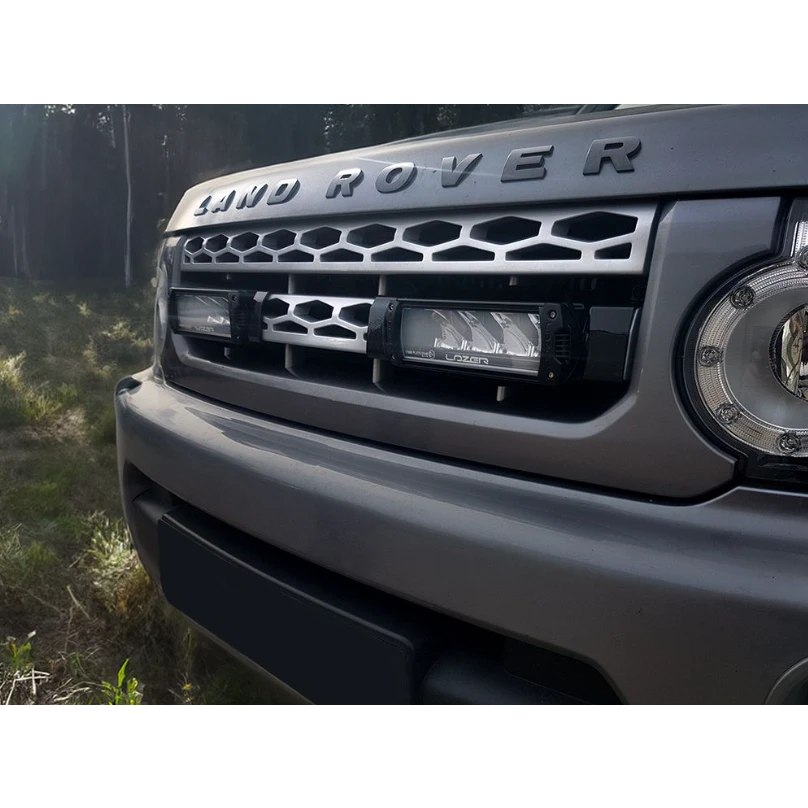 Close-up of a Land Rover vehicle's front grille and headlight in a forest setting