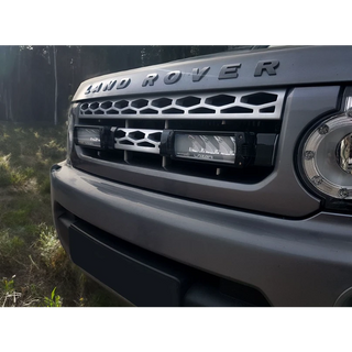 Close-up of a Land Rover vehicle's front grille and headlight in a forest setting