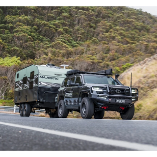 Black SUV towing a green camper trailer on a road with a mountainous background