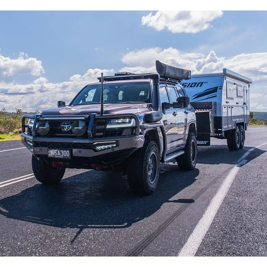 SUV towing a camper trailer on a road with a clear sky.