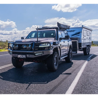 SUV towing a camper trailer on a road with a clear sky.