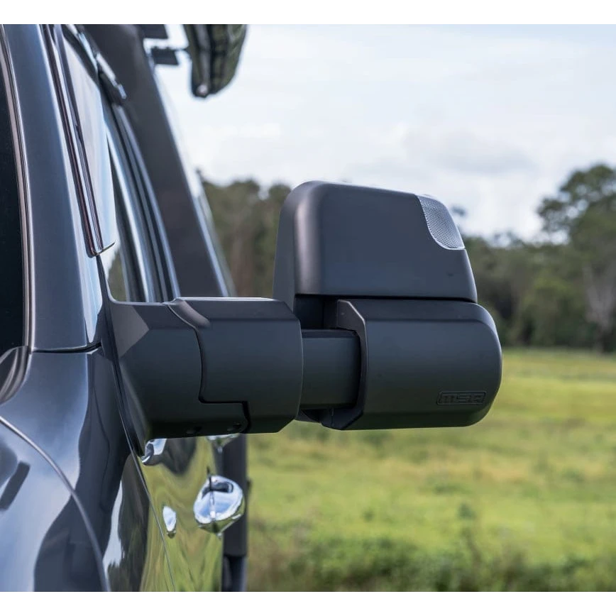 MSA Power Fold towing mirror fitted to a dark 4WD, seen from behind and to the side, the arm extended out past the body with the indicator lens in the mirror head and open paddock behind