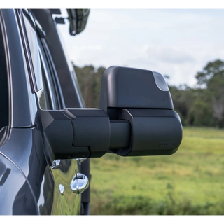 MSA Power Fold towing mirror fitted to a dark 4WD, seen from behind and to the side, the arm extended out past the body with the indicator lens in the mirror head and open paddock behind