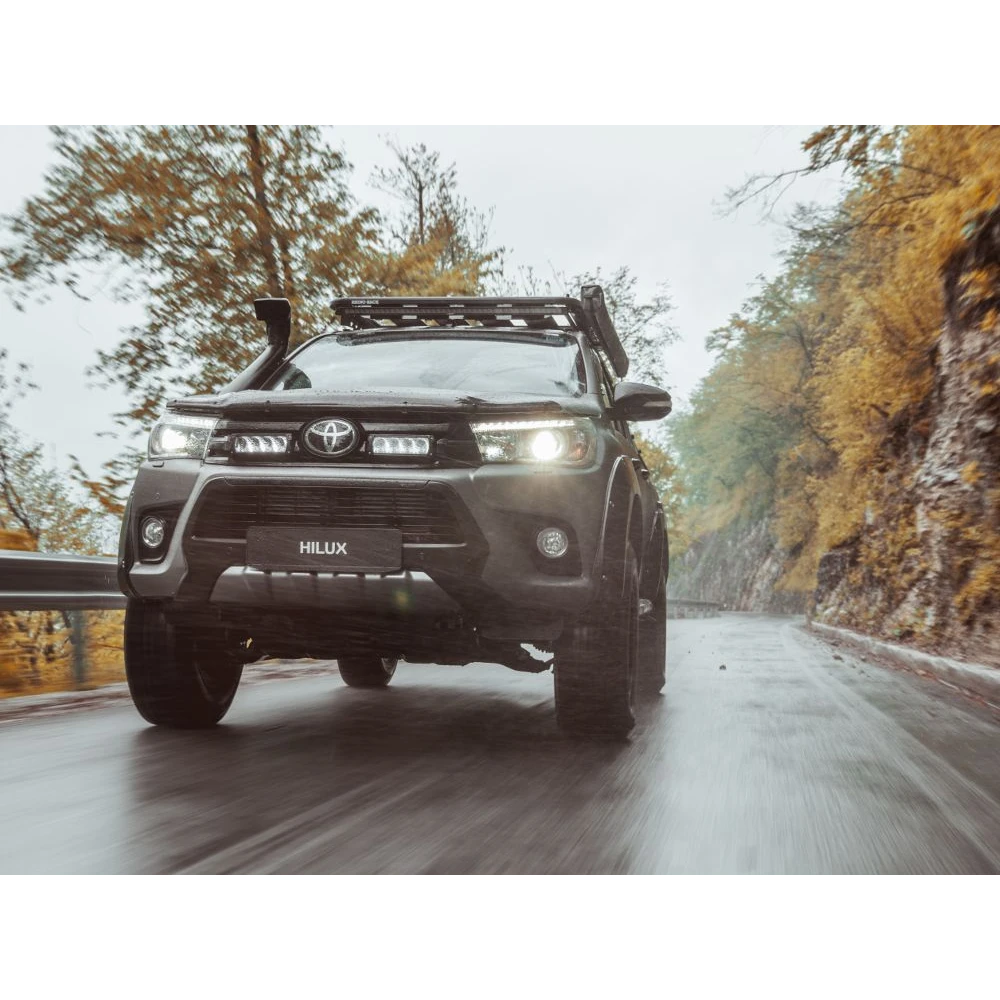 Toyota Hilux driving on a road with trees on both sides with Lazer Lamps Grille Kit for Toyota Hilux (2017-2020)