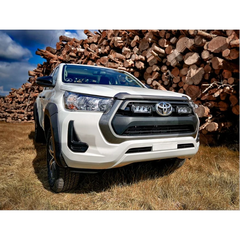 White Toyota truck parked in front of stacked wood logs with a blue sky with Lazer Lamps Grille Kit – Toyota Hilux (2021+)