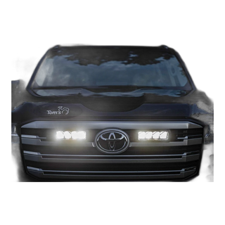 Close-up of a Toyota vehicle's front grille with illuminated headlights and Lazer Lamps Grille Kit – Toyota Land Cruiser 300 Series (2022+)