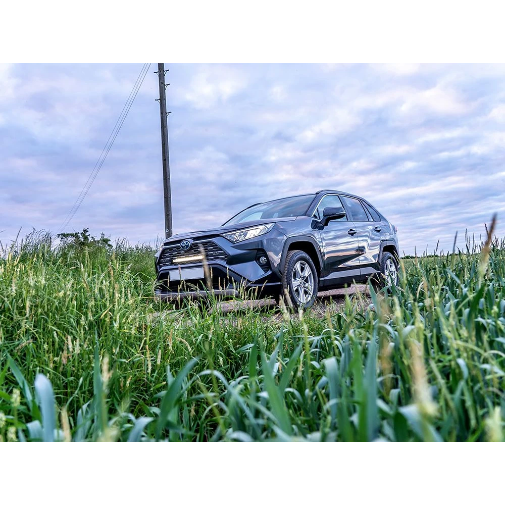 SUV driving through a grassy field with a cloudy sky with Lazer Lamps Grille Kit for Toyota RAV4 Hybrid (2019+)