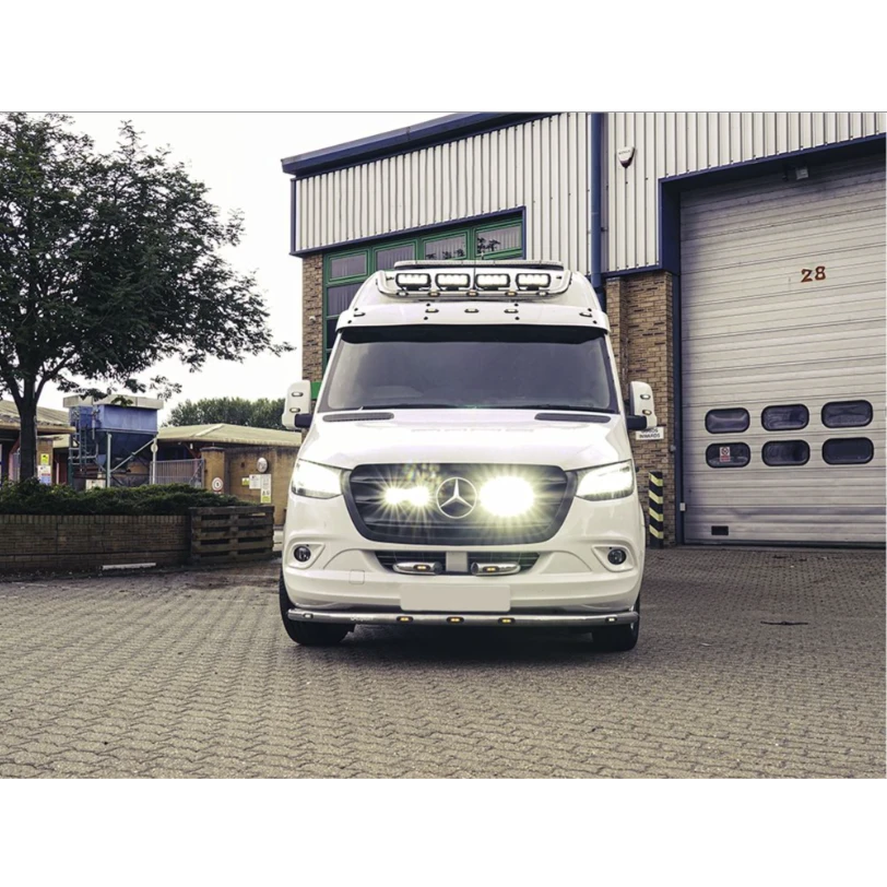 White Mercedes-Benz van parked in front of a building with a garage door with Lazer Lamps Mercedes Sprinter (2018+) Grille Kit