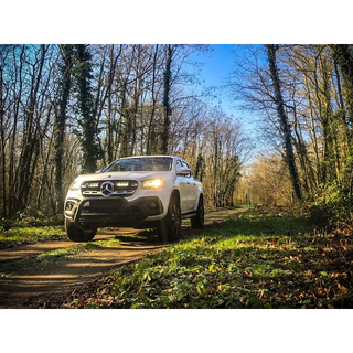Lazer Lamps Mercedes X-Class (2017+) Grille Kit – white Mercedes-Benz ute driving on a forest path with trees and grass on either side.