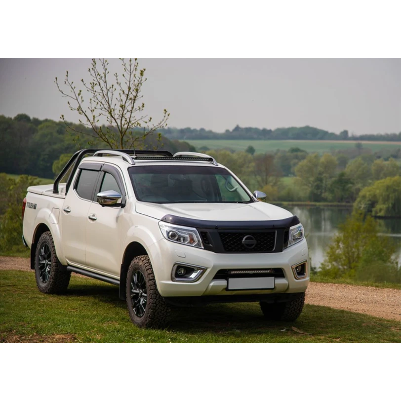 White Nissan pickup truck parked by a lake with trees in the background with Lazer Lamps Nissan Navara (2014-2019) Roof Mounting Kit