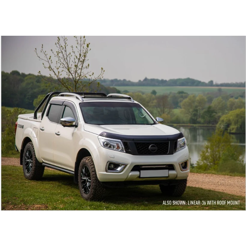 White pickup truck with roof rack parked by a lake with trees in the background