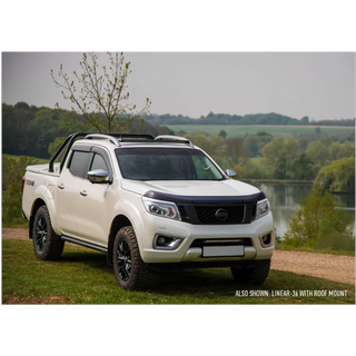 White pickup truck with roof rack parked by a lake with trees in the background