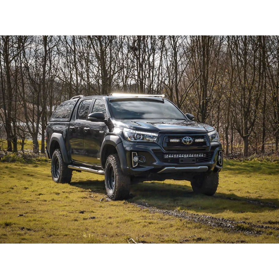 Black Toyota pickup truck on a grassy field with trees in the background with Lazer Lamps Roof Mount Kit – Toyota Hilux (2015+ No Roof Rails)