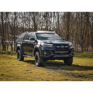 Black Toyota pickup truck on a grassy field with trees in the background with Lazer Lamps Roof Mount Kit – Toyota Hilux (2015+ No Roof Rails)