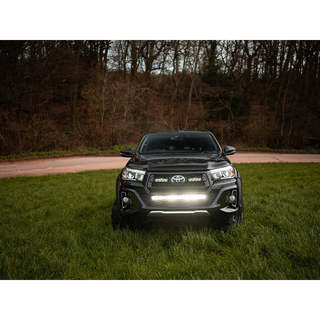 Black Toyota truck with headlights on in a grassy area with trees in the background