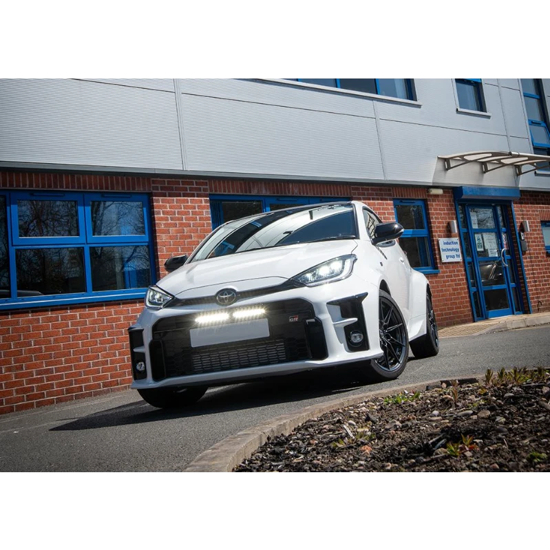 White car parked in front of a building with blue windows with Lazer Lamps Bumper Beam Mount Kit for Toyota Yaris GR