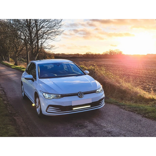 White Volkswagen car on a rural road with sunset in the background